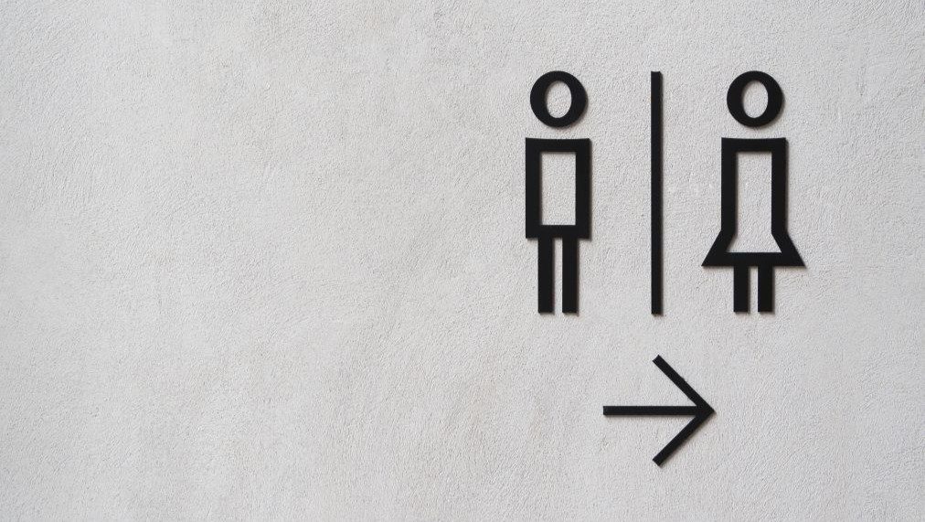 「コンクリート壁に設置された、モダンな男女トイレのサイン。ロフト風の無機質な壁面に映える公共トイレの表示。